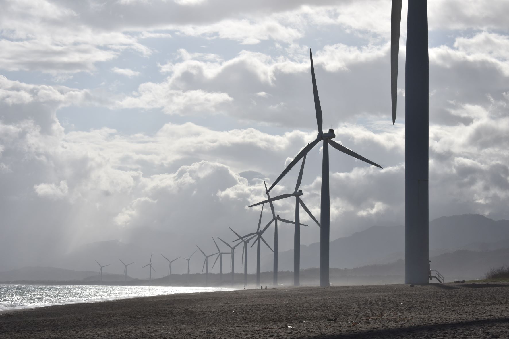 A line of wind turbines on the beach. Photo by Jem Sanchez from Pexels